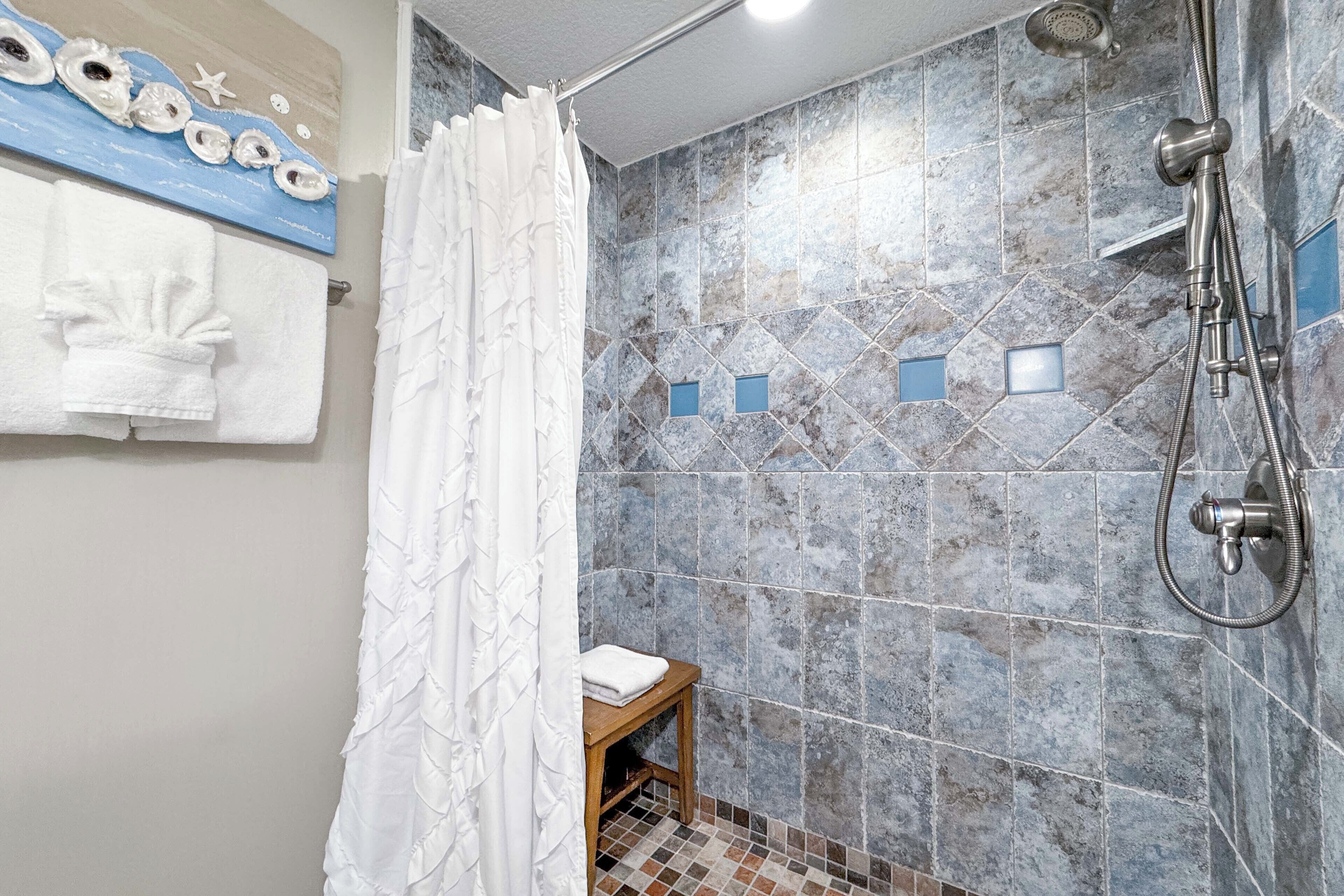 A bathroom with a shower, tiled walls, a towel rack, and a small wooden stool.