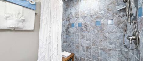 A bathroom with a shower, tiled walls, a towel rack, and a small wooden stool.
