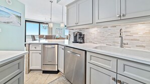 A modern kitchen with white cabinets, stainless steel appliances, and a tiled backsplash. - Summer House 501B Corner Condo | Oceanfront | Pools, Hot Tub, Tennis | My Beach Getaways (Orange Beach)
