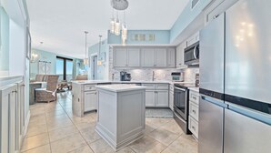 A modern kitchen with a central island, stainless steel appliances, and light blue cabinetry. - Summer House 501B Corner Condo | Oceanfront | Pools, Hot Tub, Tennis | My Beach Getaways (Orange Beach)