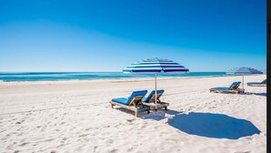 A beach with sun loungers and striped umbrellas. - Summer House 501B Corner Condo | Oceanfront | Pools, Hot Tub, Tennis | My Beach Getaways (Orange Beach)