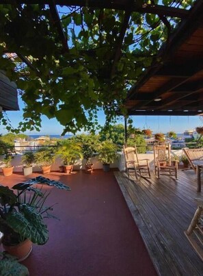 A wooden deck with potted plants and outdoor furniture, overlooking a body of water. - Casa La Maria Colonial District Two-Bedroom (Santo Domingo)