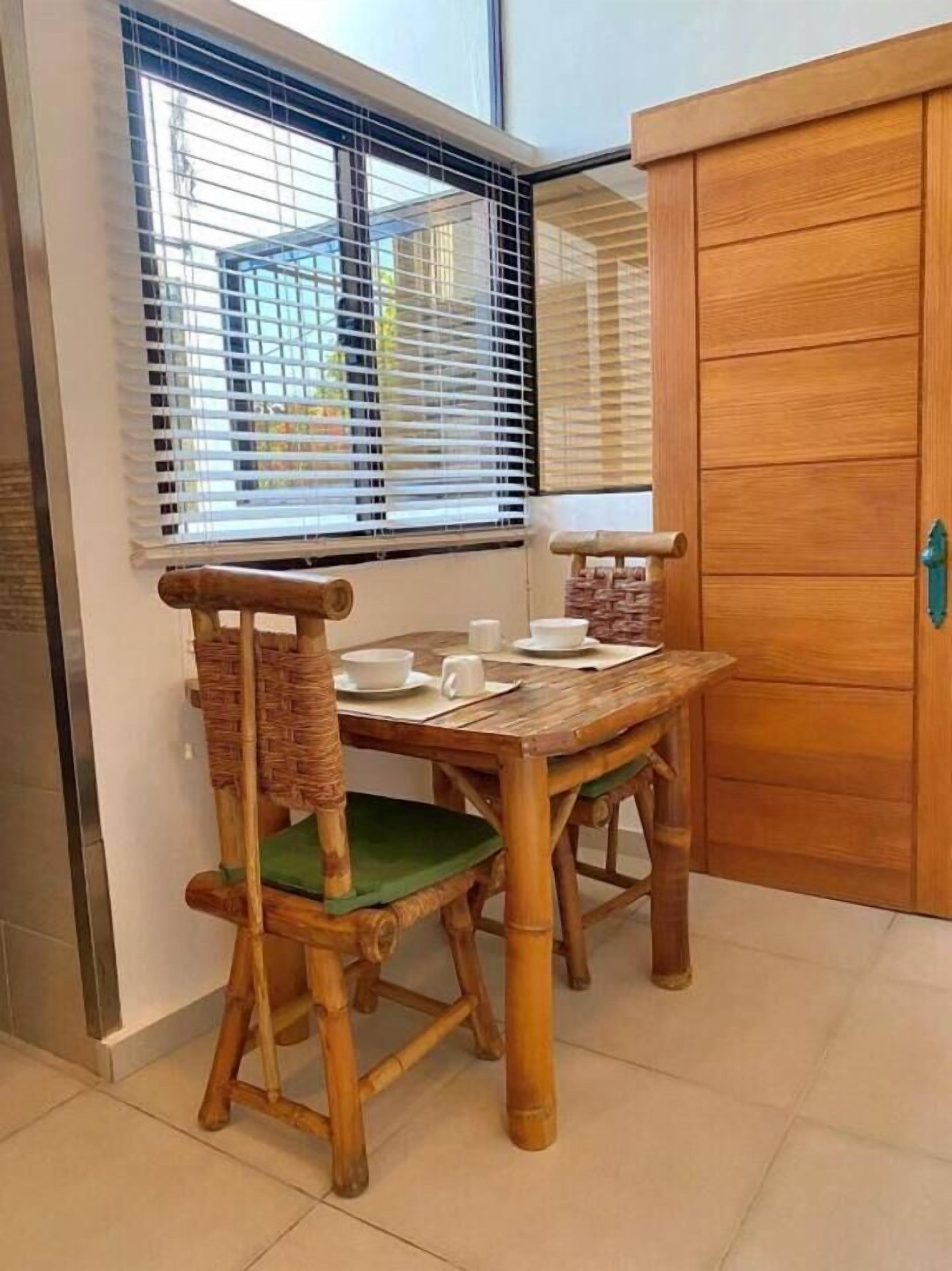 Une table de salle à manger en bois, avec des chaises, une fenêtre avec des stores et un meuble en bois.
