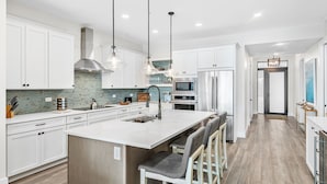 A modern kitchen with white cabinetry, a large island with bar stools, stainless steel appliances, and pendant lighting.