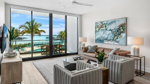 A modern living room with a large sliding glass door leading to a balcony with a pool and palm trees.