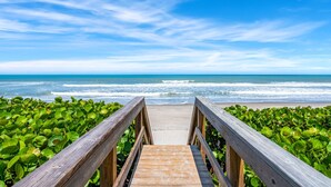 A wooden boardwalk leading to a beach with green foliage on either side.