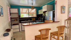 A compact kitchen with a central island, wooden chairs, and a refrigerator. - Villa Lazy Coco, a 3-minute walk from the sea (Sainte-Luce)