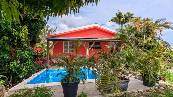 Una casa roja con piscina rodeada de abundante vegetación.