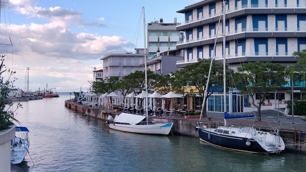A marina with boats docked, a waterfront restaurant area, and multi-story buildings with balconies. - GM001 - Gabicce, brand new studio apartment 30mt from the sea (Gabicce Mare)