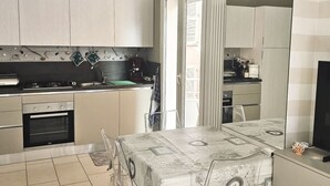 A compact kitchen with a dining area, featuring a built-in oven, a coffee machine, and a dining table with a patterned tablecloth. - GM001 - Gabicce, brand new studio apartment 30mt from the sea (Gabicce Mare)