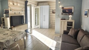 A living room with a sofa, a dining table with a patterned tablecloth, a fireplace, and a kitchen area with cabinets and a refrigerator. - GM001 - Gabicce, brand new studio apartment 30mt from the sea (Gabicce Mare)