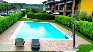 Una piscina rectangular con plataforma empedrada, dos sillones de relax y una escalera metálica.