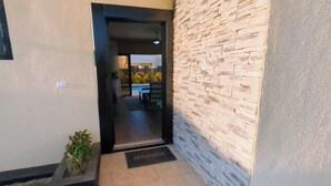 A hallway with a stone wall, a welcome mat, and a view into a dining area with a pool. - New Sunset Villa w/Private Pool - Casa Linda (Sosúa)