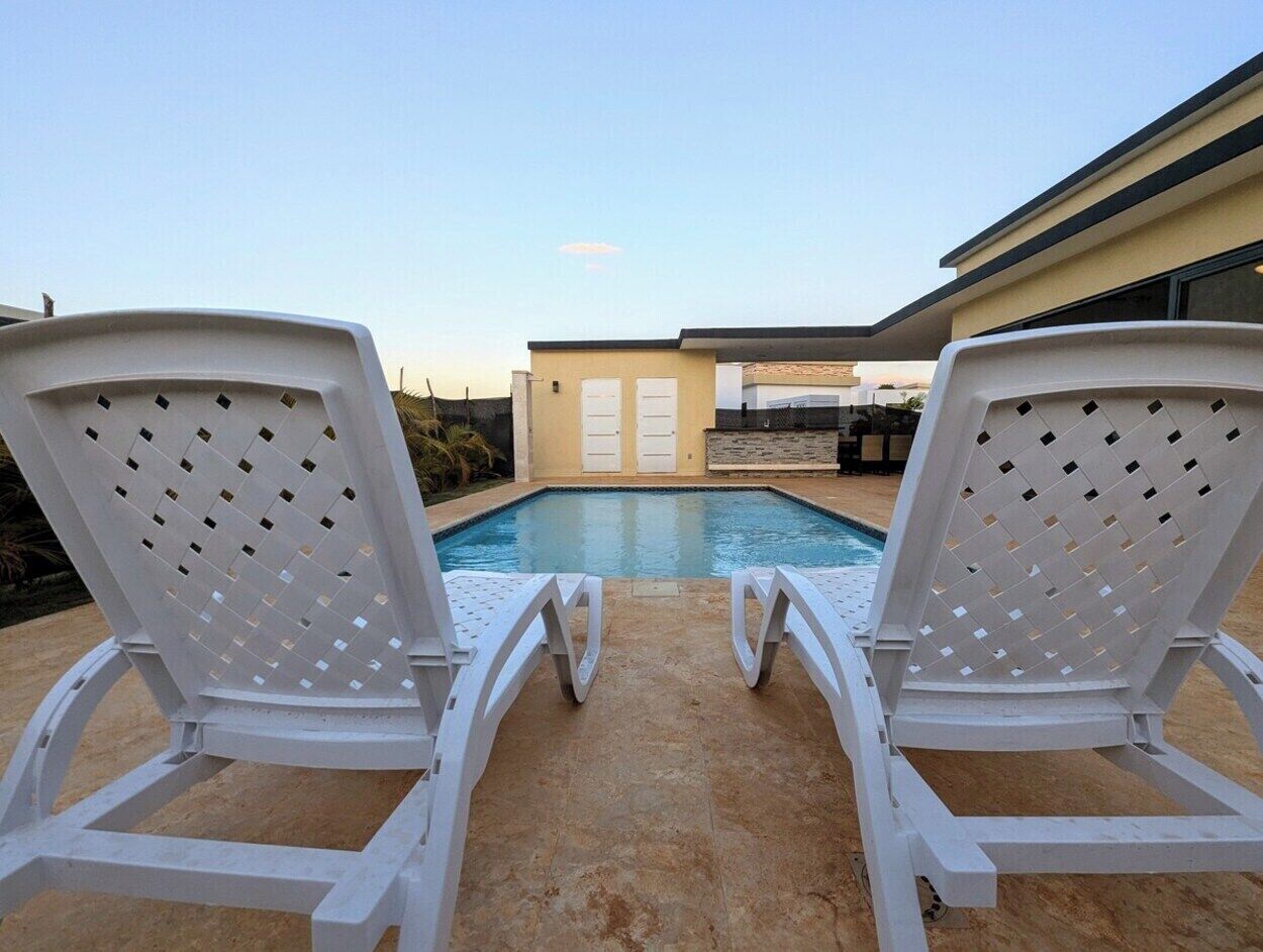 Two white lounge chairs facing a swimming pool with a building in the background.