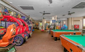 Une salle avec des tables de billard, des jeux d’arcade et des ventilateurs de plafond.