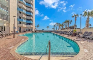 A swimming pool with lounge chairs, a building with balconies, and palm trees.