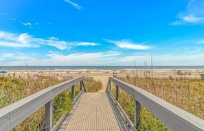 Une promenade en bois menant à une plage, avec un ciel dégagé.