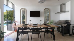 A dining area with a wooden table and black chairs, a flat-screen TV mounted on the wall, and a built-in grill.