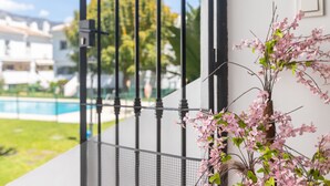 A view through a metal gate with a pool and greenery in the background.