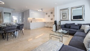 A modern living room with a grey sofa, a glass coffee table, and a dining area with a glass table and grey upholstered chairs.