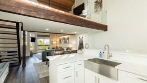 A modern kitchen with white cabinetry, a stainless steel sink, and a dining area in the background.