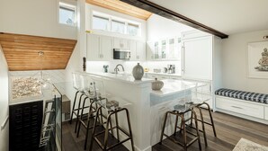 A modern kitchen with white cabinetry, a central island with stools, and a wooden ceiling.