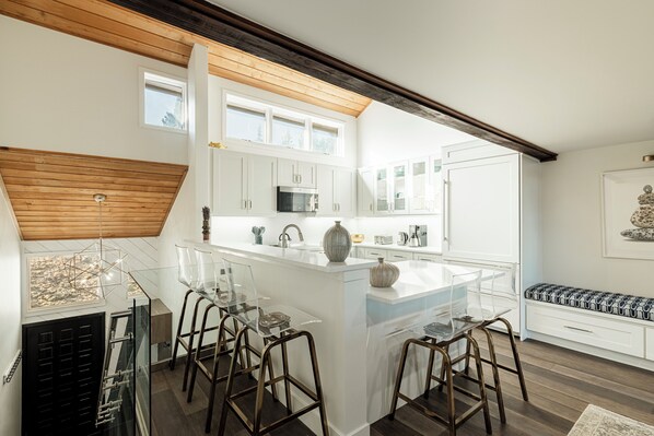 A modern kitchen with white cabinetry, a central island with stools, and a wooden ceiling.