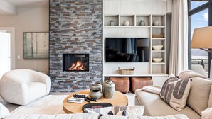 A modern living room with a brick fireplace, comfortable seating, a flat-screen TV, and a view of the outdoors.