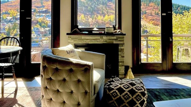 A room with a fireplace, a cushioned chair, and a view of a mountainous landscape through large windows.