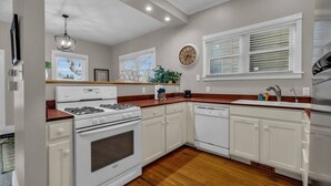 A kitchen with white cabinets, a stove, a dishwasher, and a clock on the wall.