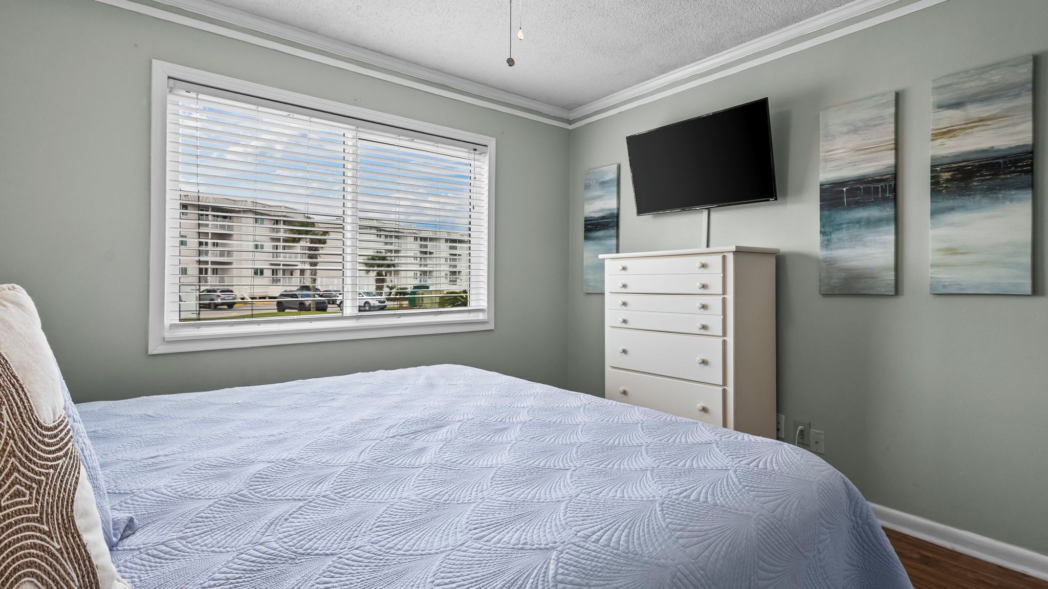 Quarto com cama, penteadeira, televisão e janela com persianas.
