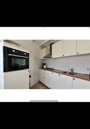 A compact kitchen with white cabinets, a black oven, and a wooden countertop. - HVD153 (4/H) Putter Recreatiewoning aan bosrand (Zwiggelte)