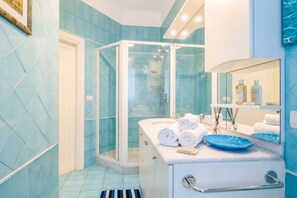 A bathroom with a glass-enclosed shower, a white sink with a blue soap dish, and a mirror above the sink. - Modern luxurious apartment to relax - city center (Bari)