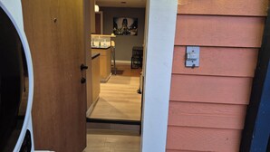 A hallway with a wooden door, a kitchen area with a sink and countertop, and a wall-mounted electrical box. - COZY GARDEN SUITE ON TRINITY STREET (Vancouver)