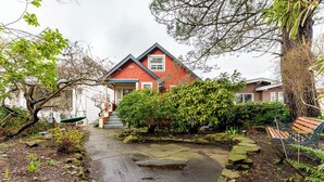 A red house with a stone pathway leading to the entrance, surrounded by greenery and a bench. - COZY GARDEN SUITE ON TRINITY STREET (Vancouver)