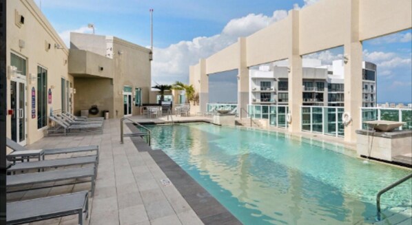 Relax by the rooftop pool surrounded by a deck and lounge chairs, offering a view of the city skyline.