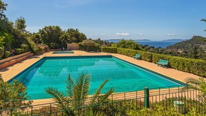 Une piscine rectangulaire à l’eau d’un bleu limpide, entourée d’une terrasse carrelée et de plantes vertes.