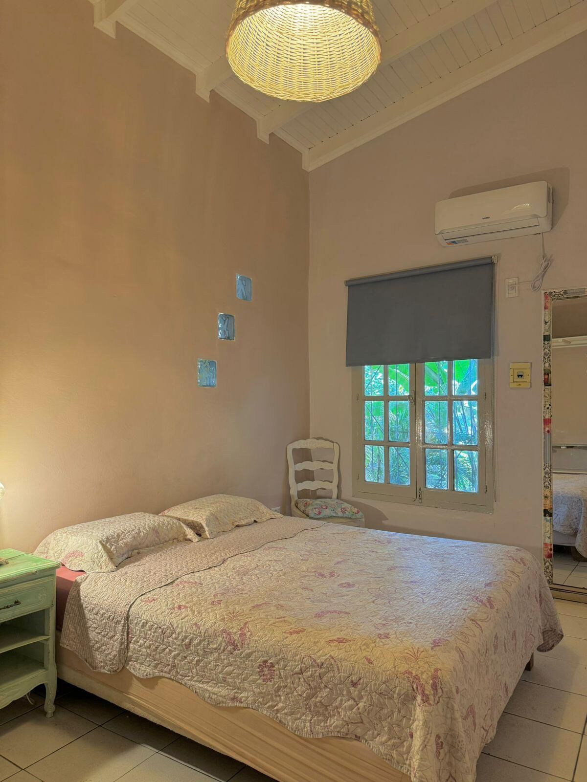 A bedroom with a bed, a chair, a window, and an air conditioning unit.