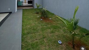 A modern building with a flat roof, a covered entrance, and a small grassy area with palm plants. - Complete House for Rest (Pedro Leopoldo)