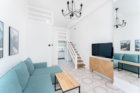 A modern living room with a sofa, TV, and staircase leading to a kitchen.