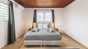 Ein Schlafzimmer mit Holzbalkendecke, einem Bett mit grauer Bettdecke, zwei Nachttischen mit Lampen und einem Fenster mit Vorhängen.