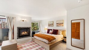 A bedroom with a fireplace, a bed, a desk, a chair, and a view of the outdoors. - Experience luxury at Alpenglow at Telluride Lodge, a spacious 2 bed/2-bath condo (Telluride)