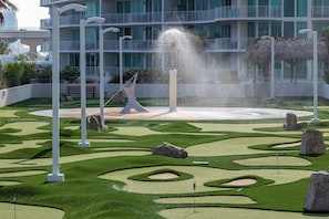 Un jardin aménagé avec une fontaine, des piliers blancs et un bâtiment doté de balcons en arrière-plan.
