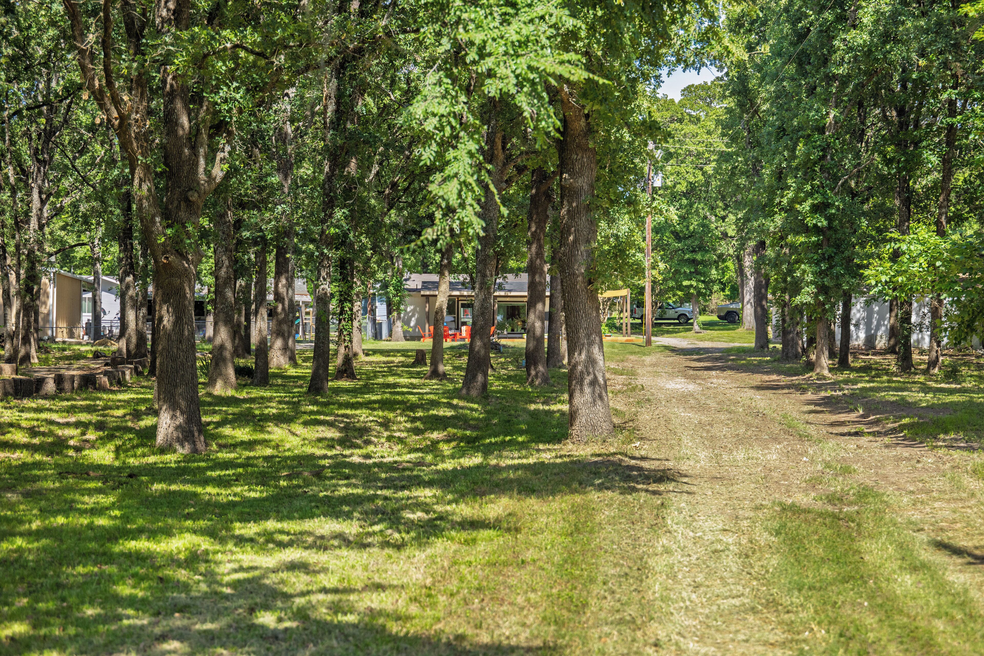 A park with a dirt path, surrounded by trees and a building in the background.
