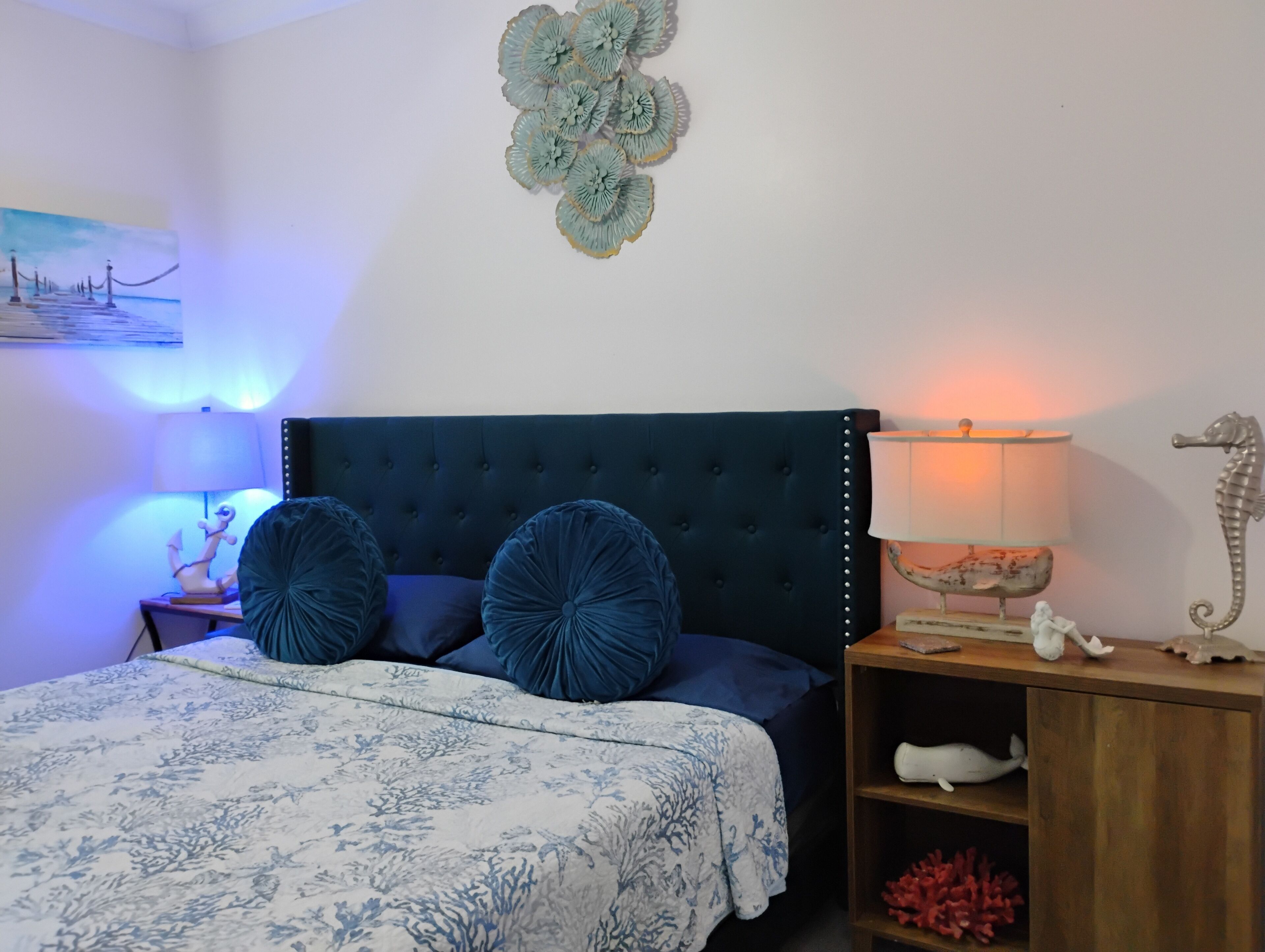 A bedroom with a dark blue tufted headboard, a floral-patterned bedspread, and two matching blue pillows.