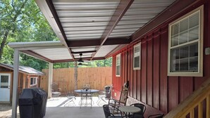 Un patio couvert équipé d’un barbecue, de meubles d’extérieur et d’une clôture en bois en arrière-plan.