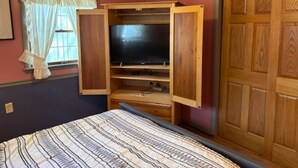 Ein Schlafzimmer mit einem Bett, einem Holzschrank, einem Fernseher und einem Fenster mit Vorhängen.