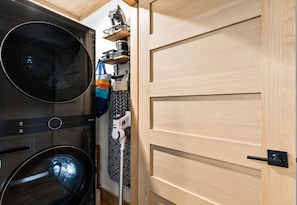 A compact laundry area with a washing machine and dryer, a drying rack, and a wooden door. - Sweet Dreams: Cozy Elegance • Hot-Tub • FireTable • Arcade Game • Mtn Views • EV (Blue Ridge)