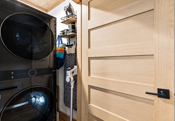 A compact laundry area with a washing machine and dryer, a drying rack, and a wooden door.