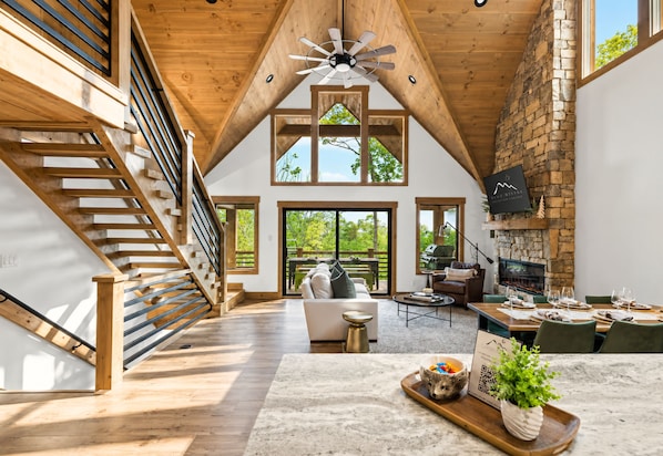 A spacious loft with a wooden staircase, a fireplace, a dining area, and large windows.